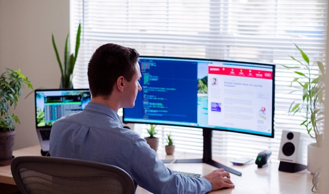 man in gray dress shirt sitting on chair in front of computer monitor